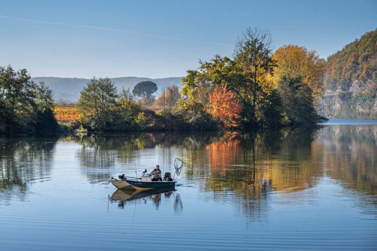 Un pêcheur en barque sur les eaux calmes de la rivière Lot en automne.